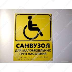 Тактильна табличка жовтого кольору з текстом санвузол для маломобільних груп населення та шрифтом Брайля фотографія на стіні