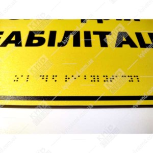 Фотографія крупним планом рельєфних точок шрифту Брайля на тактильної табличка жовтого кольору з текстом санвузол для маломобільних груп населення