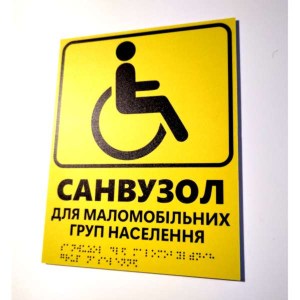 Тактильна табличка жовтого кольору з текстом санвузол для маломобільних груп населення та шрифтом Брайля фотографія праворуч
